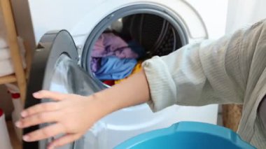 Çamaşır makinesinden çamaşırları çıkaran ve plastik havuza koyan kadın, yakın plan.