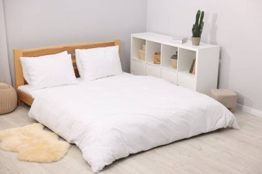 Yatak odasındaki gri duvarın yanında çarşaflı, puflu ve raflı büyük bir yatak. İç tasarım