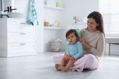 Anne banyoda bebeğinin saçını tarıyor, mesaj atmak için yer açıyor.