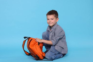 Açık mavi arka planda sırt çantası olan sevimli küçük bir çocuk.