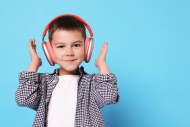Açık mavi arka planda kablosuz kulaklıklı küçük çocuk. Metin için boşluk