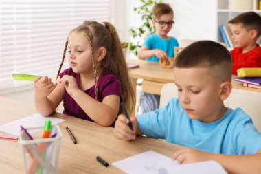 İlkokulda sanat dersi sırasında tahta masalarda oturan çocuklar.