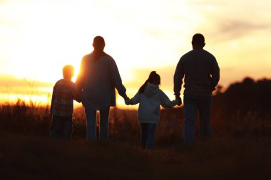 Aile gün batımında, arka planda el ele tutuşuyor.