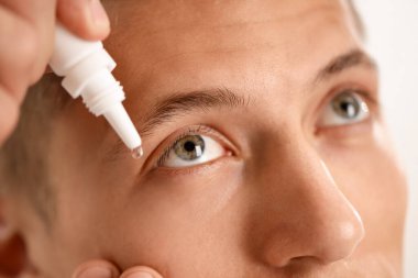 Işık arkaplanına göz damlası uygulayan adam, yakın plan