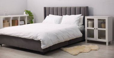 Yatak odasındaki gri duvarın yanında çarşaflı, raf üniteli ve dolaplı büyük bir yatak. İç tasarım