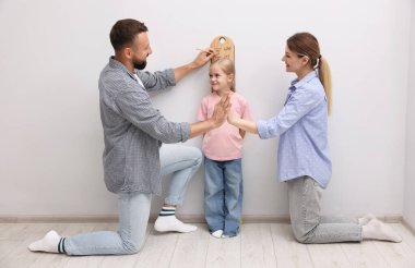 Küçük kızlarının boyunu ölçen ebeveynler beyaz duvarın yanında.