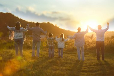Aile kucaklaşması ve yükselen eller gün batımında, arka manzara