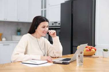 İç işlerindeki ahşap masada dizüstü bilgisayarla çalışan kulaklıklı gülen kadın.