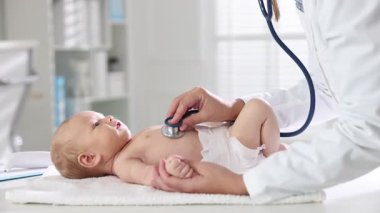 Pediyatrist hastanede steteskopla bebeği muayene ediyor.