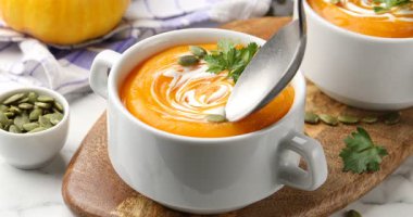 Bir kadın masadan kaşıkla balkabağı kremalı çorba alıyor, yakın plan.