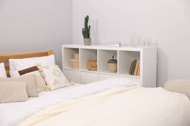 Yatak odasındaki gri duvarın yanında çarşaflı ve raf üniteli büyük bir yatak.