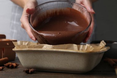 Kadın, ahşap masadaki yemek kabına çikolata hamuru döküyor, yakın plan.