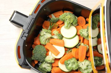 Beyaz ahşap masada çiğ havuç, brokoli ve kabak kızartma makinesi.