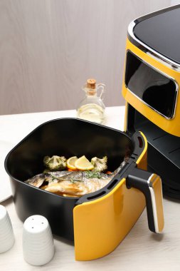 Beyaz ahşap masada pişmiş balık, limon ve sebzeler.