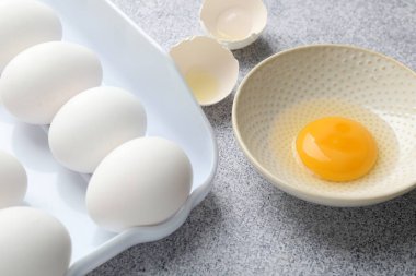 Bir sürü çiğ tavuk yumurtası ve bir tanesi gri masada kırılmış, yakın plan.