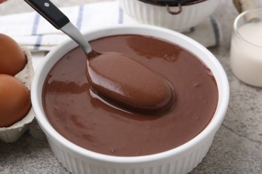 Gri masadaki kaşıkla kaseden sıvı çikolata hamuru alıyoruz. Yakın plan.