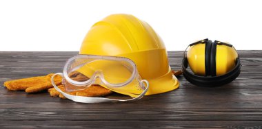 Güvenlik ekipmanları. Kasket, kulaklık, koruyucu eldivenler ve beyaz arka plana karşı ahşap masa üzerindeki gözlükler.