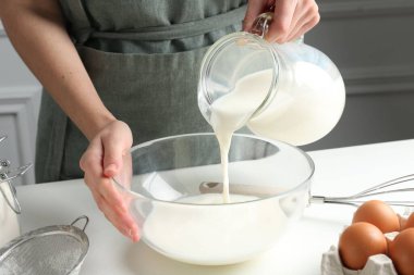 Hamur yapmak (sıvı hamur). Beyaz masadaki kaseye süt döken kadın, yakın plan.