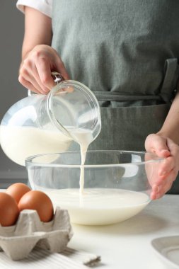 Hamur yapmak (sıvı hamur). Beyaz masadaki kaseye süt döken kadın, yakın plan.