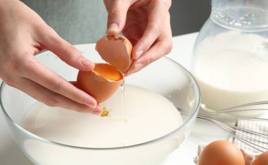 Hamur yapmak (sıvı hamur). Beyaz masadaki kaseye yumurta ekleyen kadın, yakın plan.