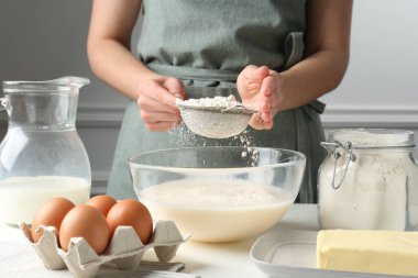 Hamur yapmak (sıvı hamur). Beyaz masada un yiyen bir kadın. Kapalı alanda, yakın plan.
