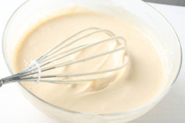 Beyaz masa üzerinde hamurlu kase ve çırpma (sıvı hamur), yakın plan