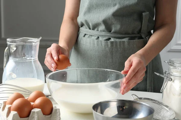 Hamur yapmak (sıvı hamur). Beyaz masadaki kaseye yumurta ekleyen kadın, yakın plan.