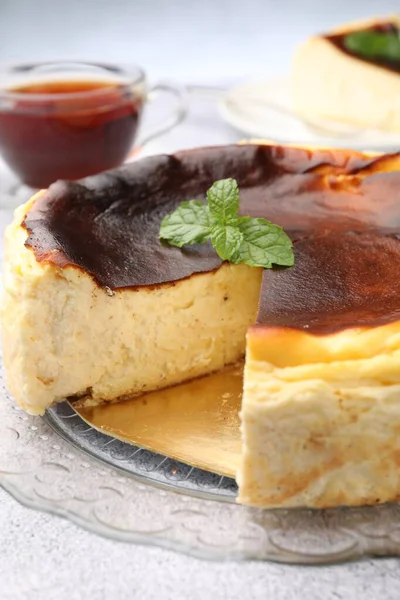 Delicious Basque cheesecake with mint and tea on light grey table, closeup