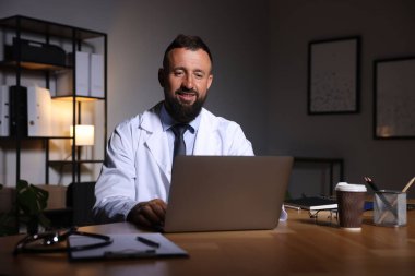 Doktor, gece vardiyası sırasında klinikteki masada dizüstü bilgisayarla çalışıyor.