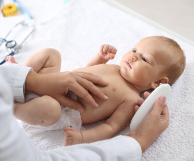 Pediyatrist bebeğin sıcaklığını hastanede termometreyle ölçüyor.