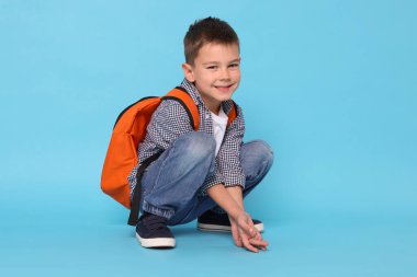 Açık mavi arka planda sırt çantası olan sevimli küçük bir çocuk.