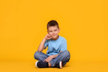 Turuncu arka planda oturan sevimli küçük çocuk.