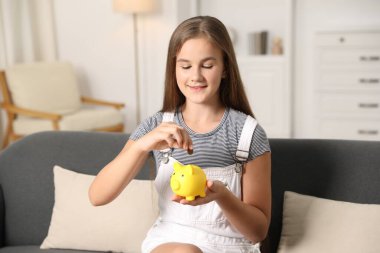 Kız cep harçlığını evdeki kanepedeki kumbaraya yatırıyor.