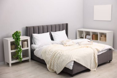 Yatak odasındaki gri duvarın yanında çarşaflı, raf üniteli ve dolaplı büyük bir yatak. İç tasarım