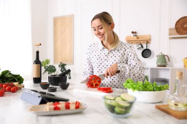 Mutfakta yemek pişirirken tabletten yemek tarifine bakan gülümseyen kadın.