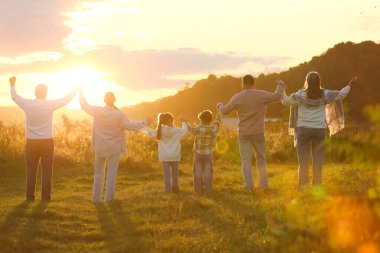 Aile kucaklaşması ve yükselen eller gün batımında, arka manzara