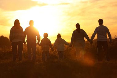 Aile gün batımında, arka planda el ele tutuşuyor.