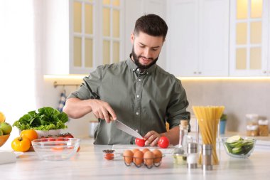 Yemek pişirme süreci. Gülümseyen adam mutfakta domates kesiyor.