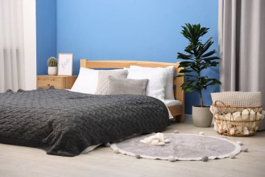 Yatak odasındaki mavi duvarın yanında çarşaflı, komodinli, sepetli büyük bir yatak. İç tasarım