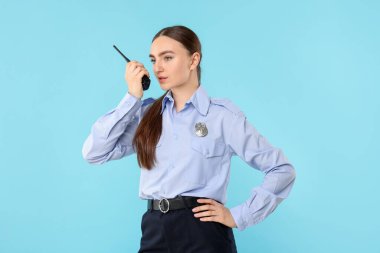 Açık mavi arka planda telsizi olan üniformalı genç bir kadın polis.