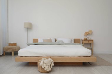 Yatak odasındaki beyaz duvarın yanında çarşafları, mobilyaları ve lambaları olan rahat büyük bir yatak.