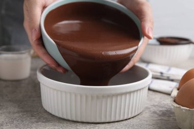 Gri masadaki yemek kabına çikolata hamuru döken kadın, yakın plan.