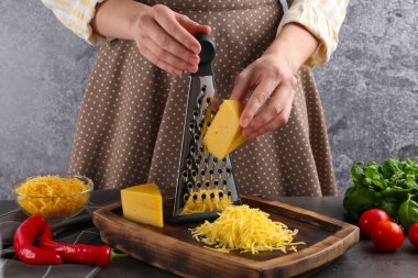 Gri masada peynir rendeleyen kadın, yakın plan.