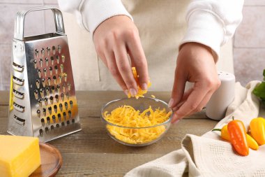 Ahşap masada rendelenmiş peynirli kadın, yakın plan.