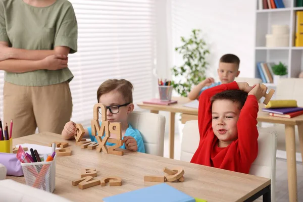 İlkokulda tahta masalarda öğretmenden ders alan küçük çocuklar, yakın çekim.