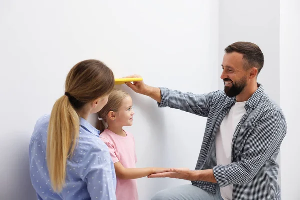 Ebeveynler küçük kızlarının boyunu içeride beyaz bir duvarın yanında ölçüyorlar.