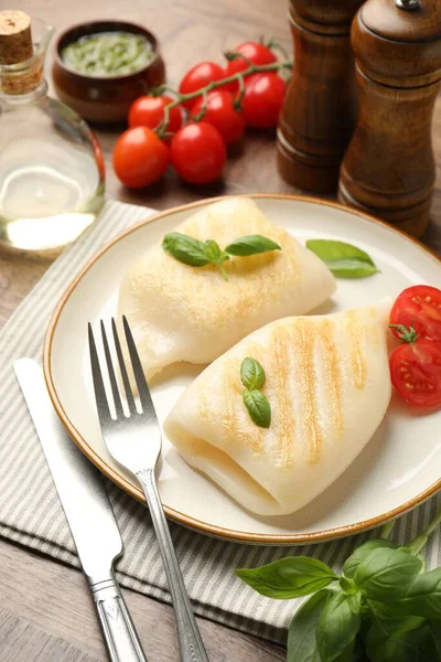 Lezzetli ızgara kalamar, domates, fesleğen ve çatal bıçak parçaları ahşap masada, yakın plan.