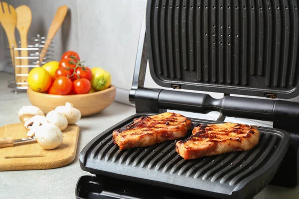 Mutfaktaki ışık masasında nefis biftek ve sebzelerle elektrikli ızgara.