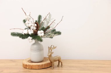 Vazoda köknar ağacı dalları ve beyaz duvarın yakınındaki ahşap masada ren geyiği figürleriyle güzel bir kompozisyon, yazı için yer. Kış Dekorasyonu
