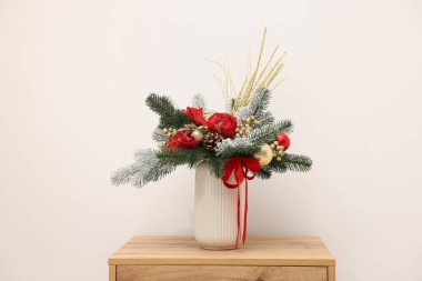 Beyaz duvarın yanındaki ahşap masada, vazoda köknar ağacı dalları olan güzel bir kompozisyon. Kış Dekorasyonu